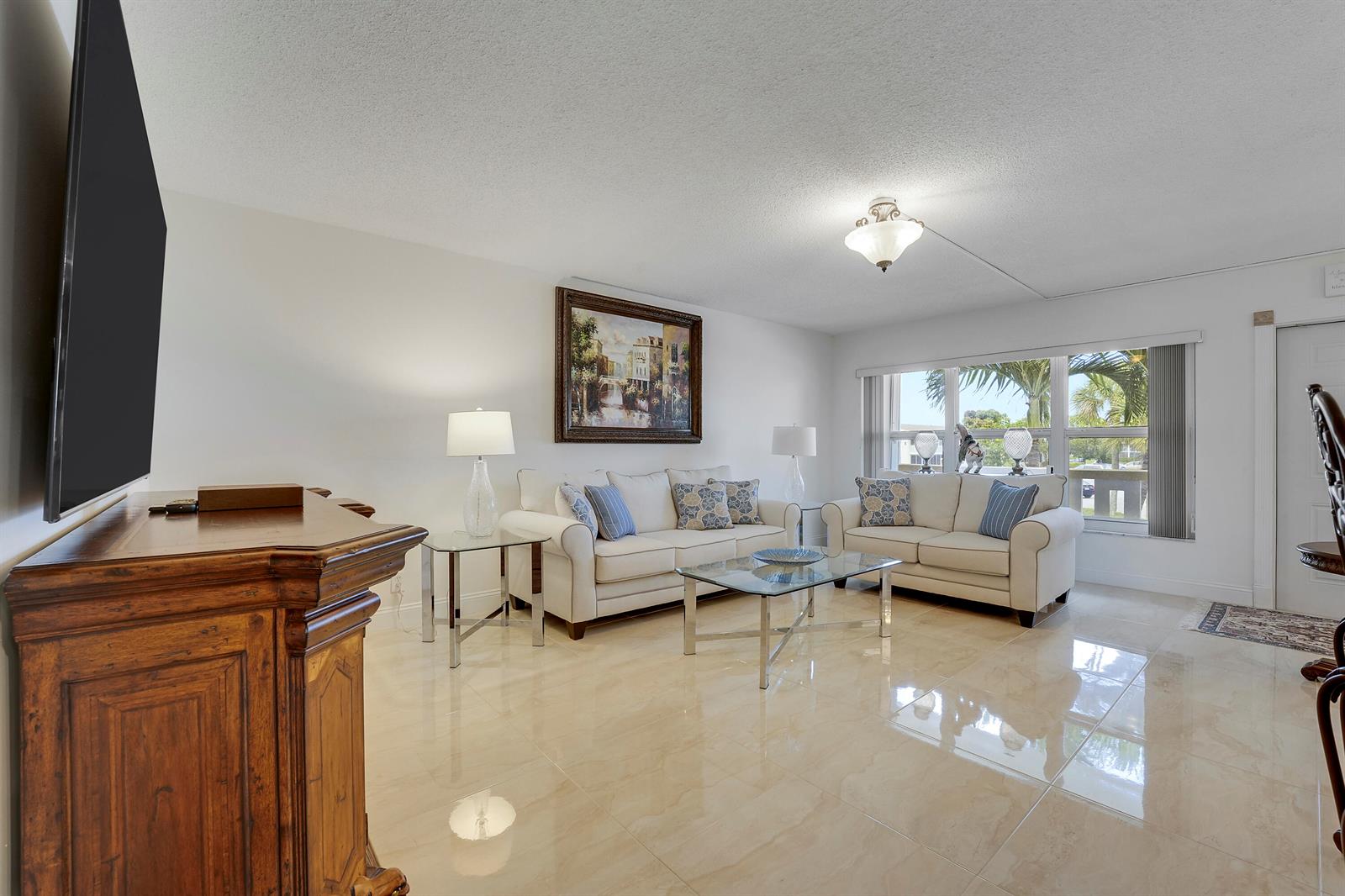 A bright living room features light tile floors, two white sofas, and a large window — 210 Wellington E, West Palm Beach FL 33417, WEST PALM BEACH, FL
