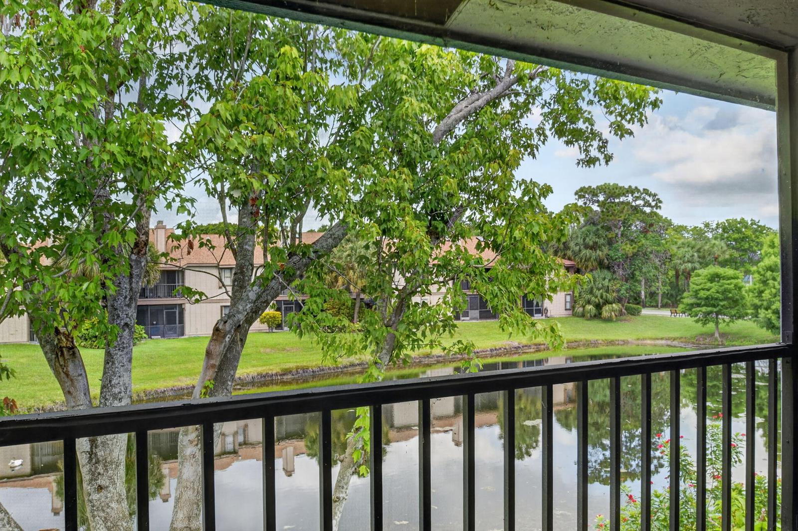 A view from a balcony overlooking a pond, green lawn, and apartment buildings — 907 Harbour Pointe Way, FL 33413, FL