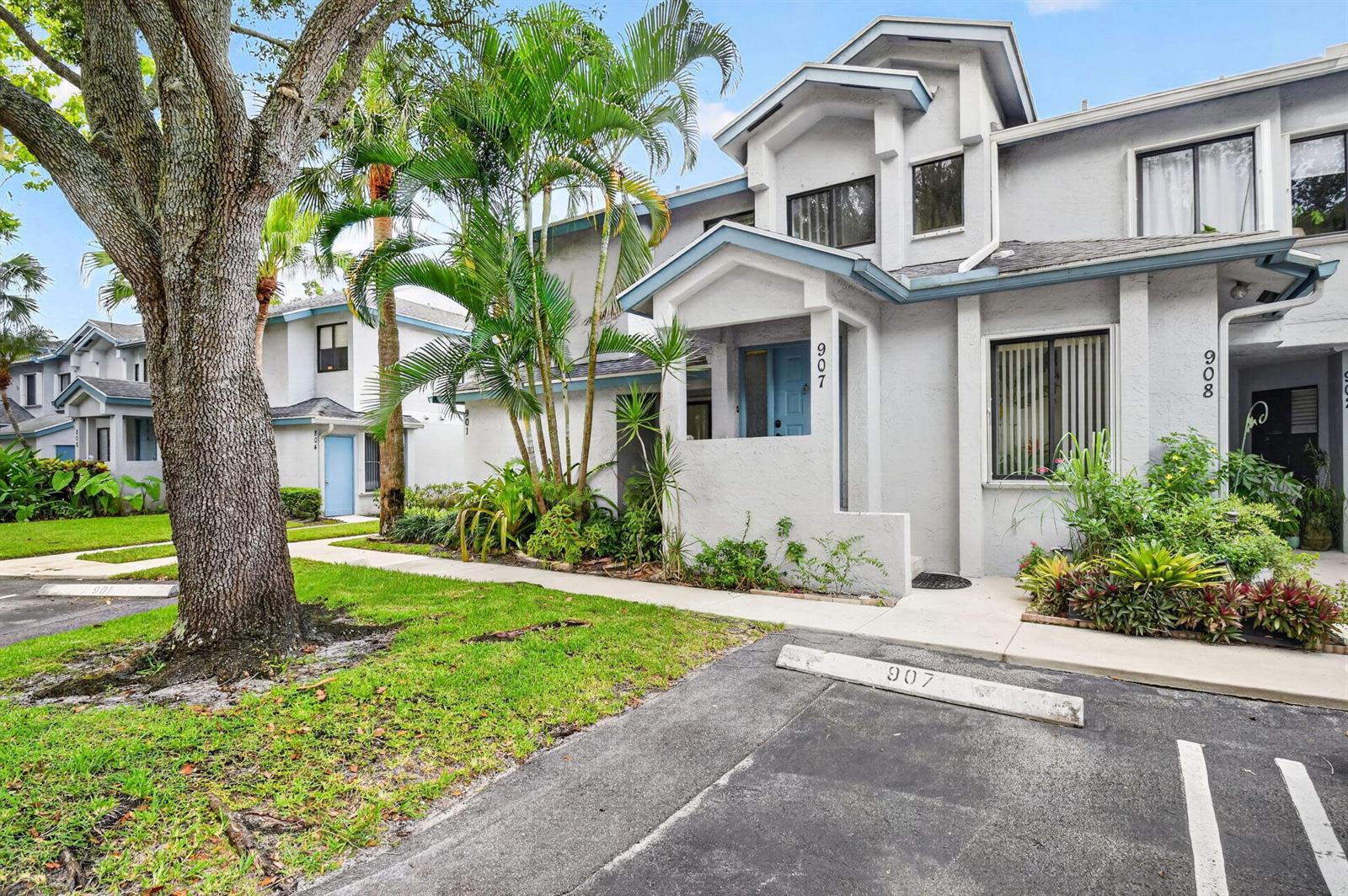Exterior view of two-story townhomes with light gray stucco walls and assigned parking spaces — 907 Harbour Pointe Way, FL 33413, FL