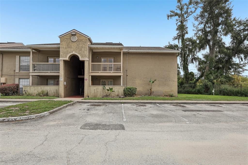 A two-story apartment building with tan stucco siding and a parking lot in front — 305 WYMORE ROAD UNIT 208, ALTAMONTE SPRINGS, FL