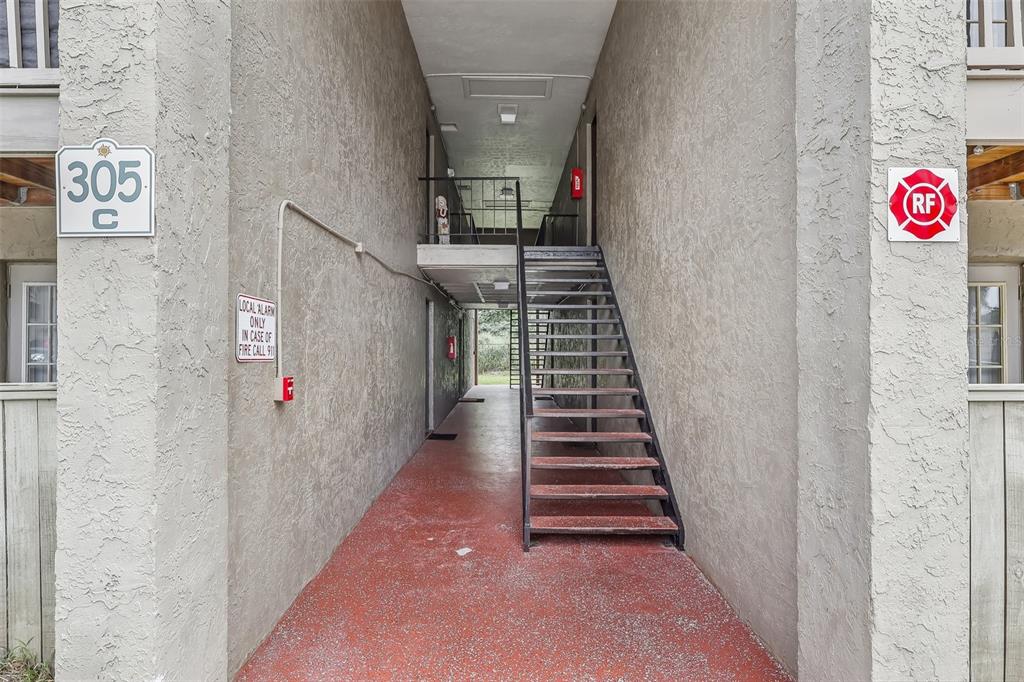 An outdoor stairwell leads to an upper level between two stucco apartment building walls — 305 WYMORE ROAD UNIT 208, ALTAMONTE SPRINGS, FL
