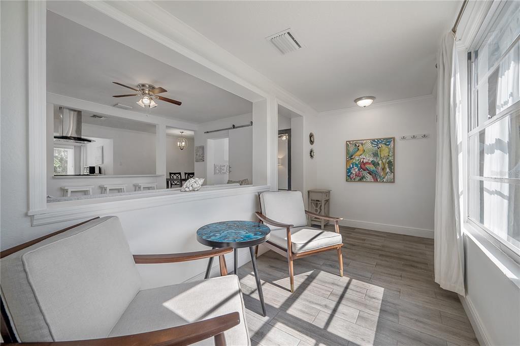 A sunlit sitting area features two armchairs, a small round table, and wood-look tile flooring — 7204 N 15TH STREET, TAMPA, FL