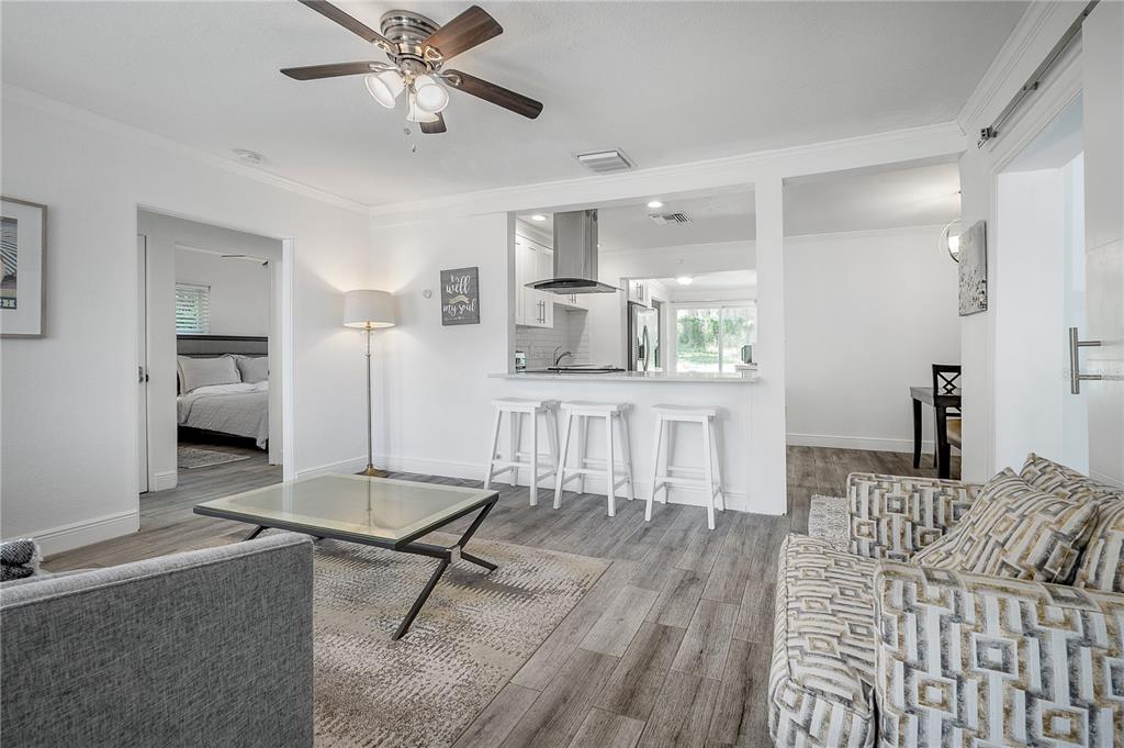 A living room with gray wood-look flooring, a glass coffee table, and a kitchen breakfast bar — 7204 N 15TH STREET, TAMPA, FL