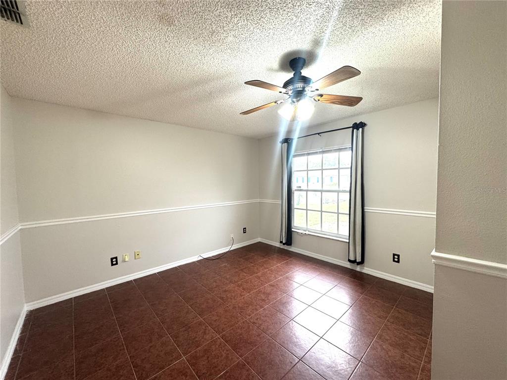 An empty room with brown tile flooring, white walls, chair rail molding, and a ceiling fan — 2728 CORRIGAN DRIVE, DELTONA, FL