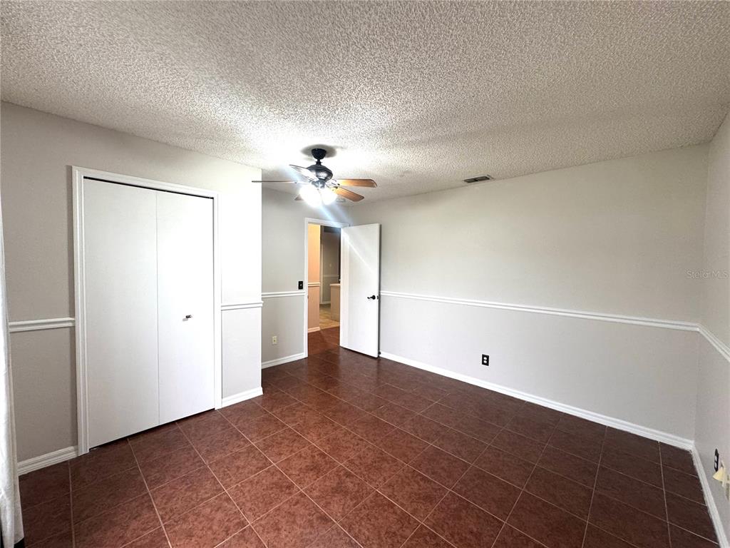 An empty room features brown tile flooring, white walls with chair rail molding, and a ceiling fan — 2728 CORRIGAN DRIVE, DELTONA, FL