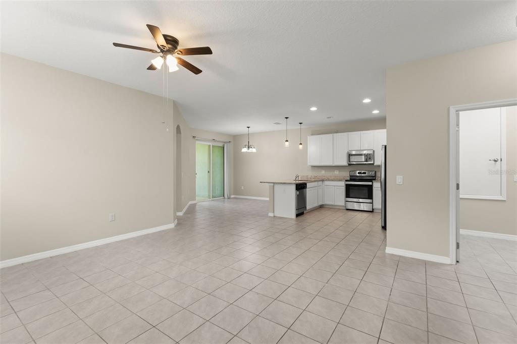 An open-concept living area with tile flooring, a ceiling fan, and a kitchen with white cabinets — 1858 SHUMARD AVENUE, ST CLOUD, FL