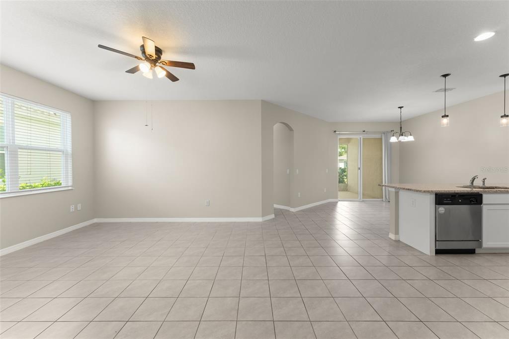 An open-concept living and dining area features tile flooring, a ceiling fan, and kitchen access — 1858 SHUMARD AVENUE, ST CLOUD, FL