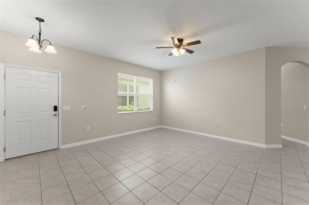 An empty room features light-colored tile flooring, beige walls, a ceiling fan, and a window — 1858 SHUMARD AVENUE, ST CLOUD, FL