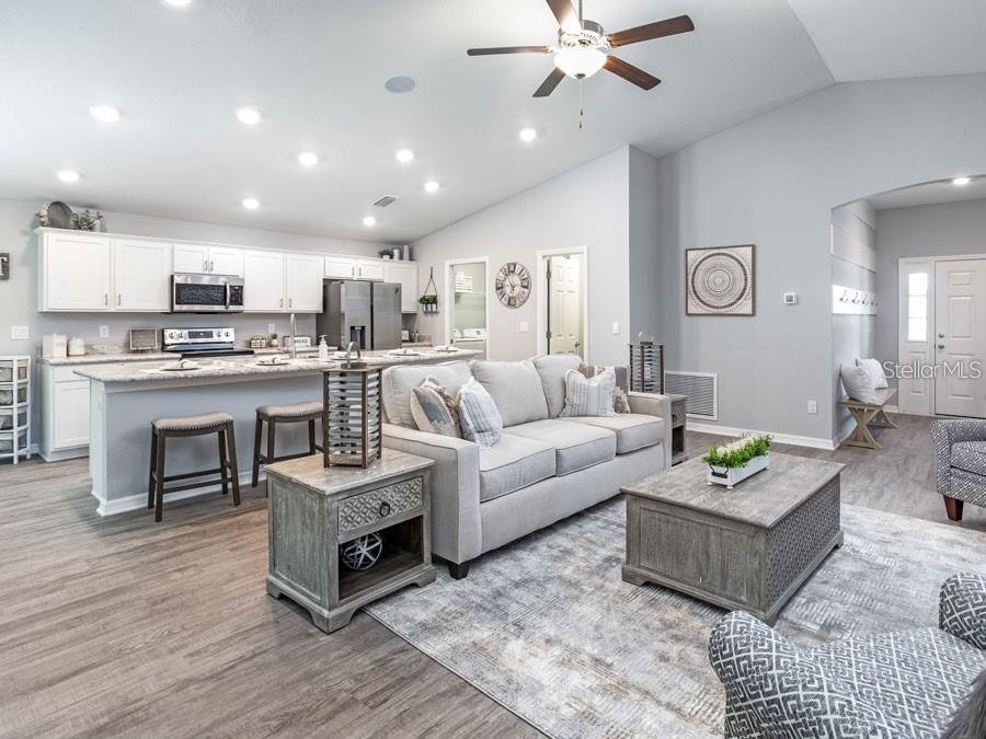 An open-concept living room and kitchen featuring light gray walls, white cabinetry, and wood-look flooring — 1821 NOBLE DRIVE, DAVENPORT, FL