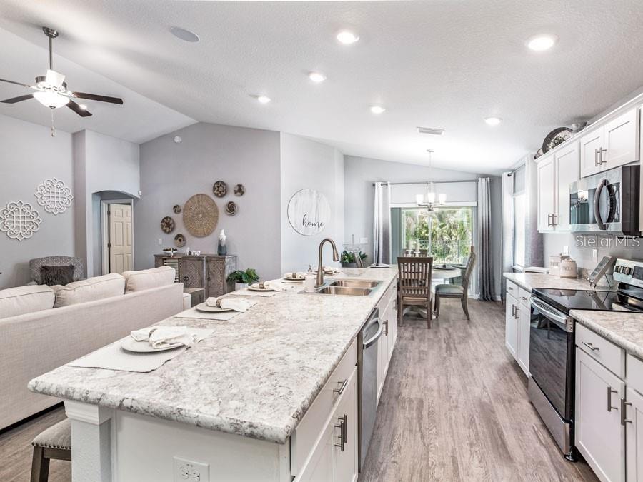 A kitchen with a large granite island, white cabinets, and stainless steel appliances opens to a living area — 1821 NOBLE DRIVE, DAVENPORT, FL