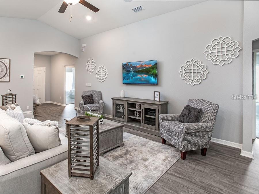 A living room features gray walls, wood-look flooring, a mounted television, and patterned armchairs — 1821 NOBLE DRIVE, DAVENPORT, FL