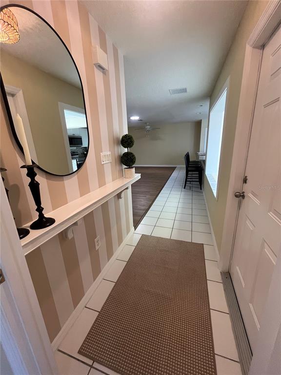 A hallway features striped wallpaper, a mirror, a shelf, and tile flooring leading to a room — 1111 APPLE TERRACE, LEESBURG, FL