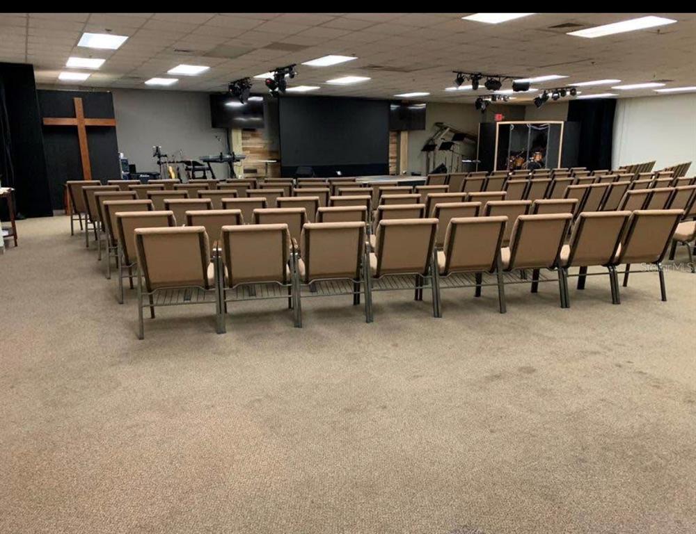 A church sanctuary features rows of tan chairs facing a stage with a large cross — 7540 GRAND AVE, WINTER PARK, FL