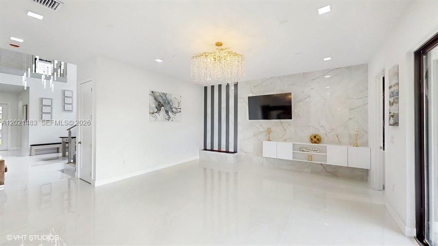 A modern living room features white tile floors, a marble accent wall, and a chandelier — 8350 Royal County Down Rd, Boca Raton FL 33434, BOCA RATON, FL