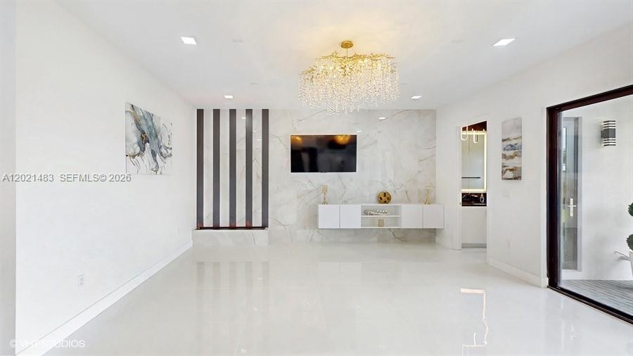 A modern living room features white marble walls, a gold chandelier, and a television — 8350 Royal County Down Rd, Boca Raton FL 33434, BOCA RATON, FL