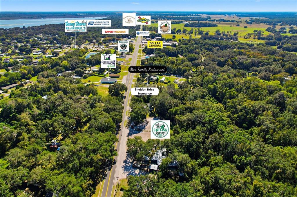 This aerial view shows a rural road lined with businesses and trees near a lake — 2339 N COUNTY 470 ROAD, LAKE PANASOFFKEE, FL