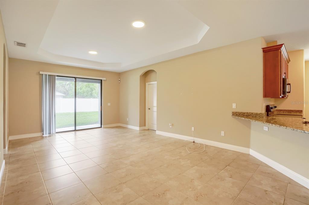 A living room with tile flooring, a tray ceiling, and sliding glass doors to a yard — 12690 VANDER WAY, NEW PORT RICHEY, FL