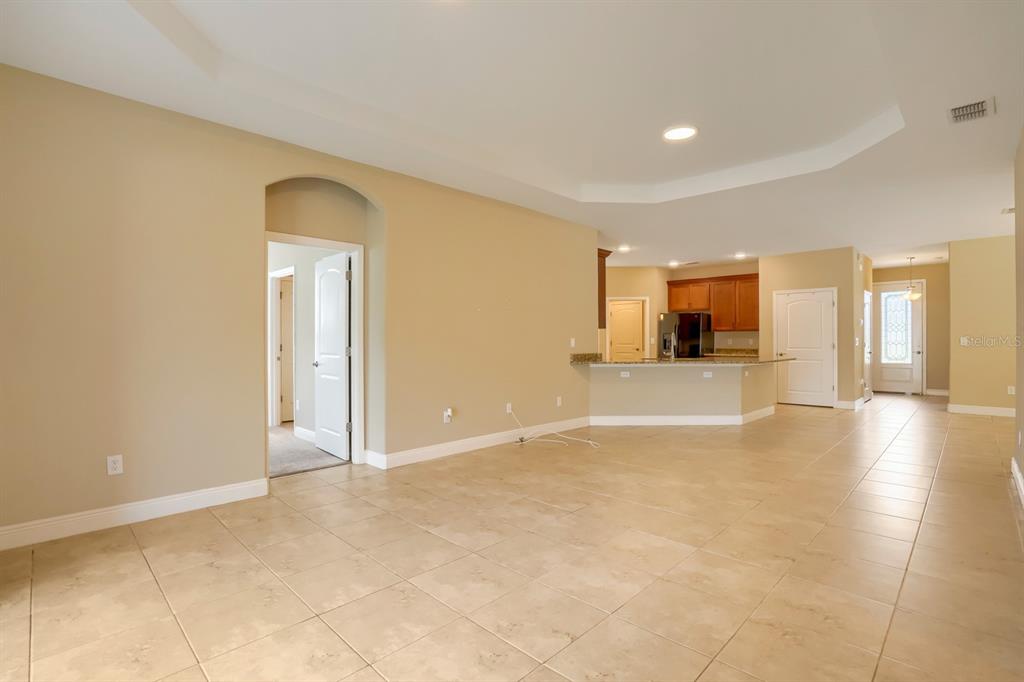 An open-concept living area with tile flooring, a tray ceiling, and an adjacent kitchen — 12690 VANDER WAY, NEW PORT RICHEY, FL