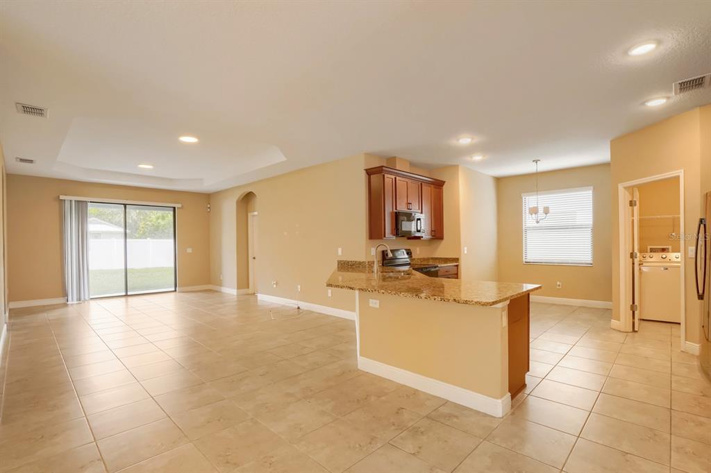 An open-concept kitchen with granite countertops overlooks a living area with tile flooring — 12690 VANDER WAY, NEW PORT RICHEY, FL