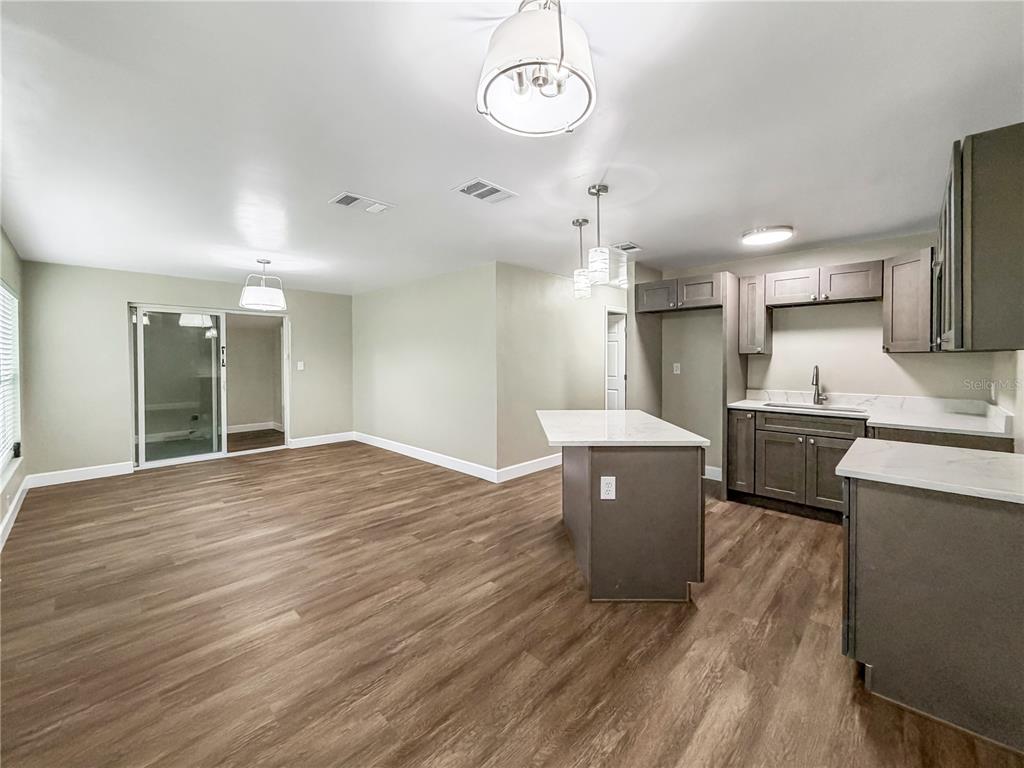 An open-concept kitchen and dining area features dark gray cabinets, white countertops, and wood-look flooring — 4228 KIRKLAND BOULEVARD, ORLANDO, FL