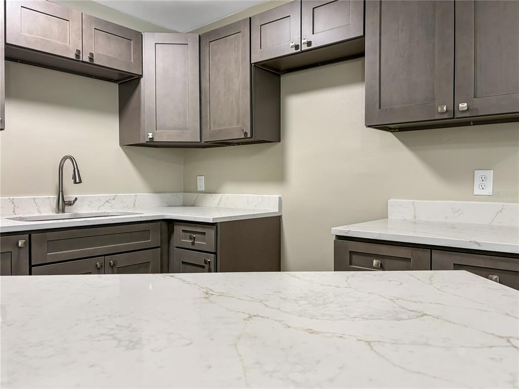 A kitchen features dark wood cabinets, white marble-look countertops, and a stainless steel sink — 4228 KIRKLAND BOULEVARD, ORLANDO, FL