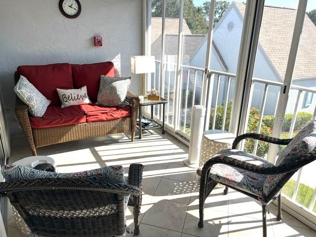 A sunroom features wicker furniture with red and patterned cushions overlooking a residential neighborhood — 6713 STONE RIVER RD UNIT 203, BRADENTON, FL