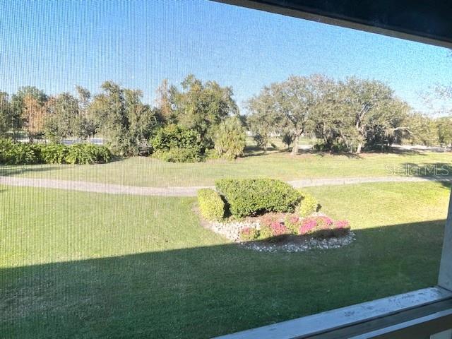 A view of a grassy lawn and landscaping seen through a screened-in porch window — 6713 STONE RIVER RD UNIT 203, BRADENTON, FL