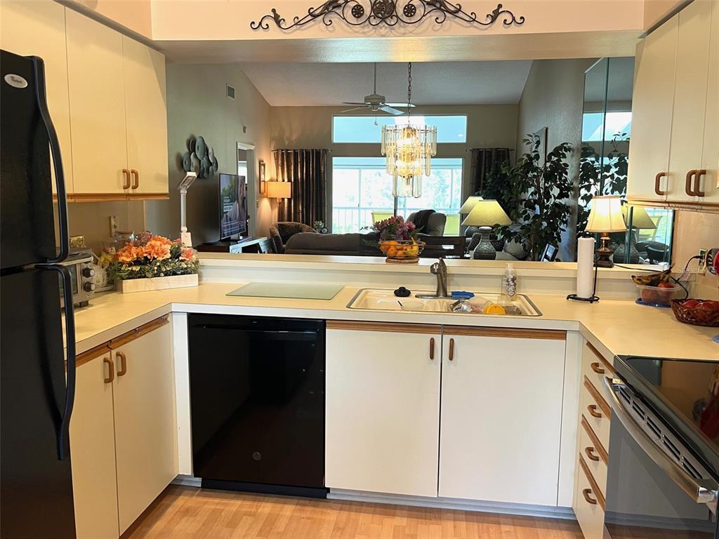 A kitchen with white cabinets, black appliances, and a pass-through window overlooking the living area — 6713 STONE RIVER RD UNIT 203, BRADENTON, FL