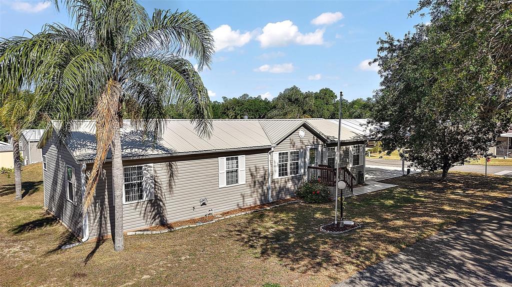 A single-story manufactured home with light siding, a metal roof, and an attached carport — 37945 MONTICELLO STREET, LEESBURG, FL