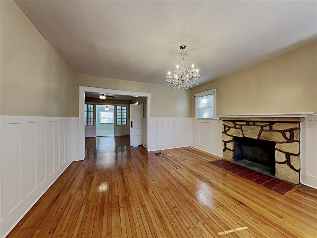 A living room features hardwood floors, white wainscoting, a stone fireplace, and a crystal chandelier — 628 N HALIFAX AVENUE, DAYTONA BEACH, FL