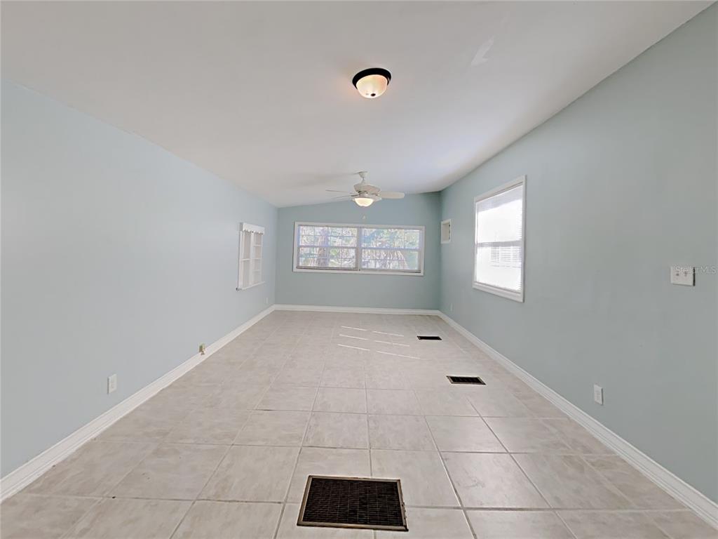 A spacious room with light blue walls, tile flooring, a ceiling fan, and multiple windows — 628 N HALIFAX AVENUE, DAYTONA BEACH, FL