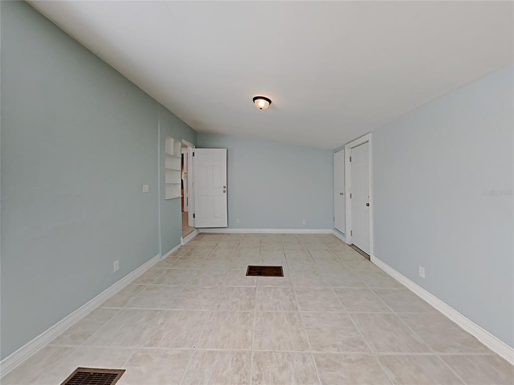 A room with light blue walls, beige tile flooring, a central ceiling light, and two doors — 628 N HALIFAX AVENUE, DAYTONA BEACH, FL