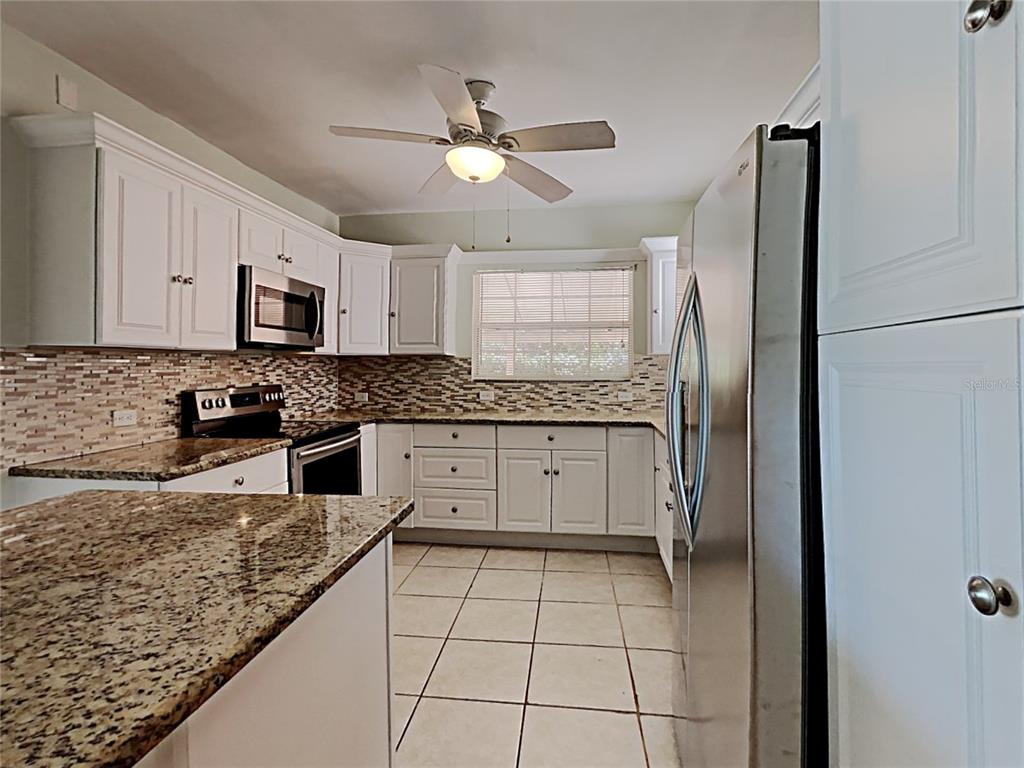 A kitchen features white cabinets, granite countertops, stainless steel appliances, and a tiled floor — 628 N HALIFAX AVENUE, DAYTONA BEACH, FL