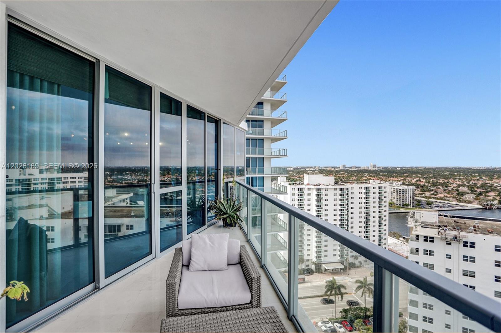 A high-rise balcony features a wicker chair, glass railings, and expansive city and water views — 3101 S Ocean Dr, Hollywood FL 33019, HOLLYWOOD, FL