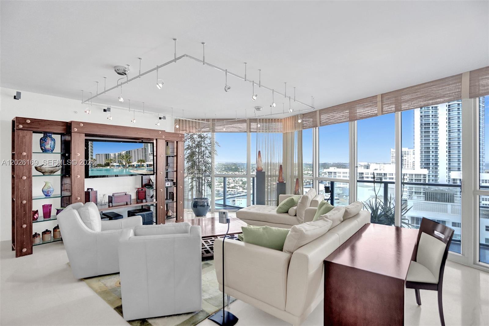 A modern living room features a large entertainment unit, white sofas, and floor-to-ceiling windows — 3101 S Ocean Dr, Hollywood FL 33019, HOLLYWOOD, FL