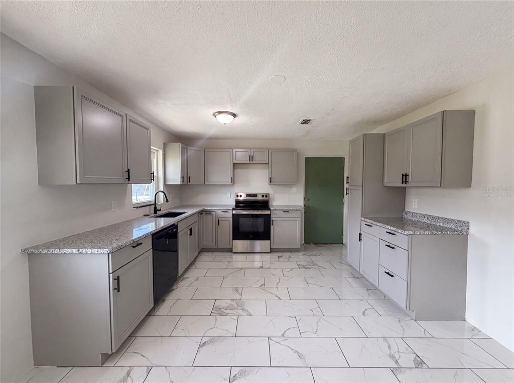 A kitchen features gray cabinets, granite countertops, stainless steel appliances, and white marble-look tile flooring — 417 CALUMET ROAD, AVON PARK, FL
