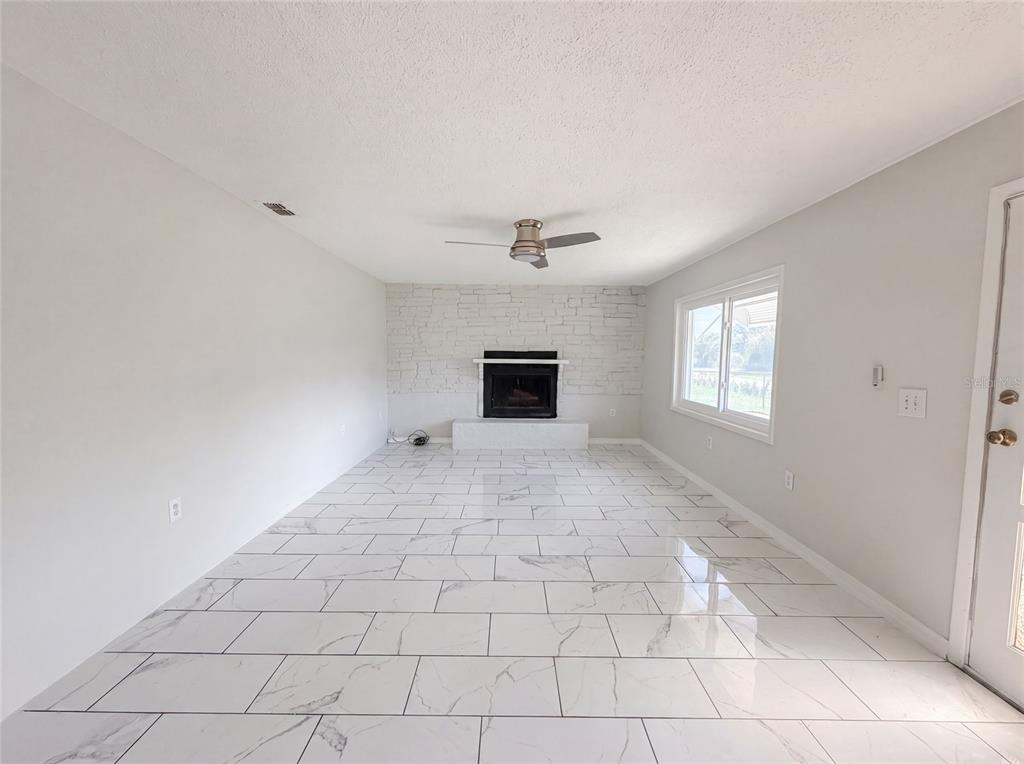 A living room features white marble-look tile flooring, a white stone fireplace, and a ceiling fan — 417 CALUMET ROAD, AVON PARK, FL