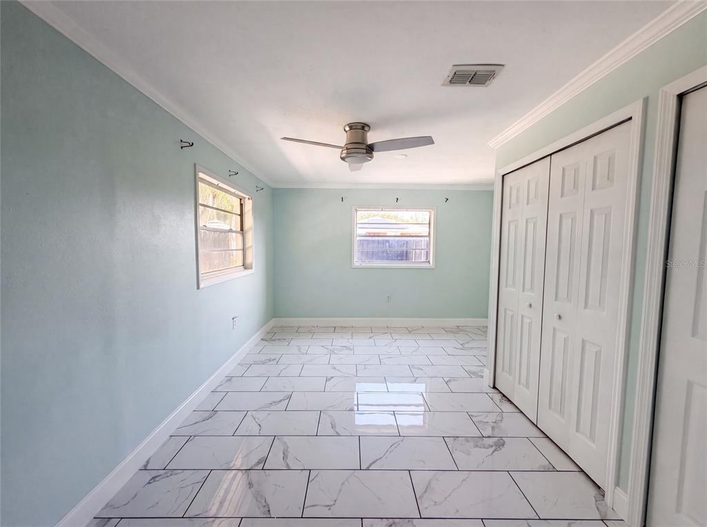 A room with light blue walls, white marble-look tile flooring, a ceiling fan, and closets — 417 CALUMET ROAD, AVON PARK, FL