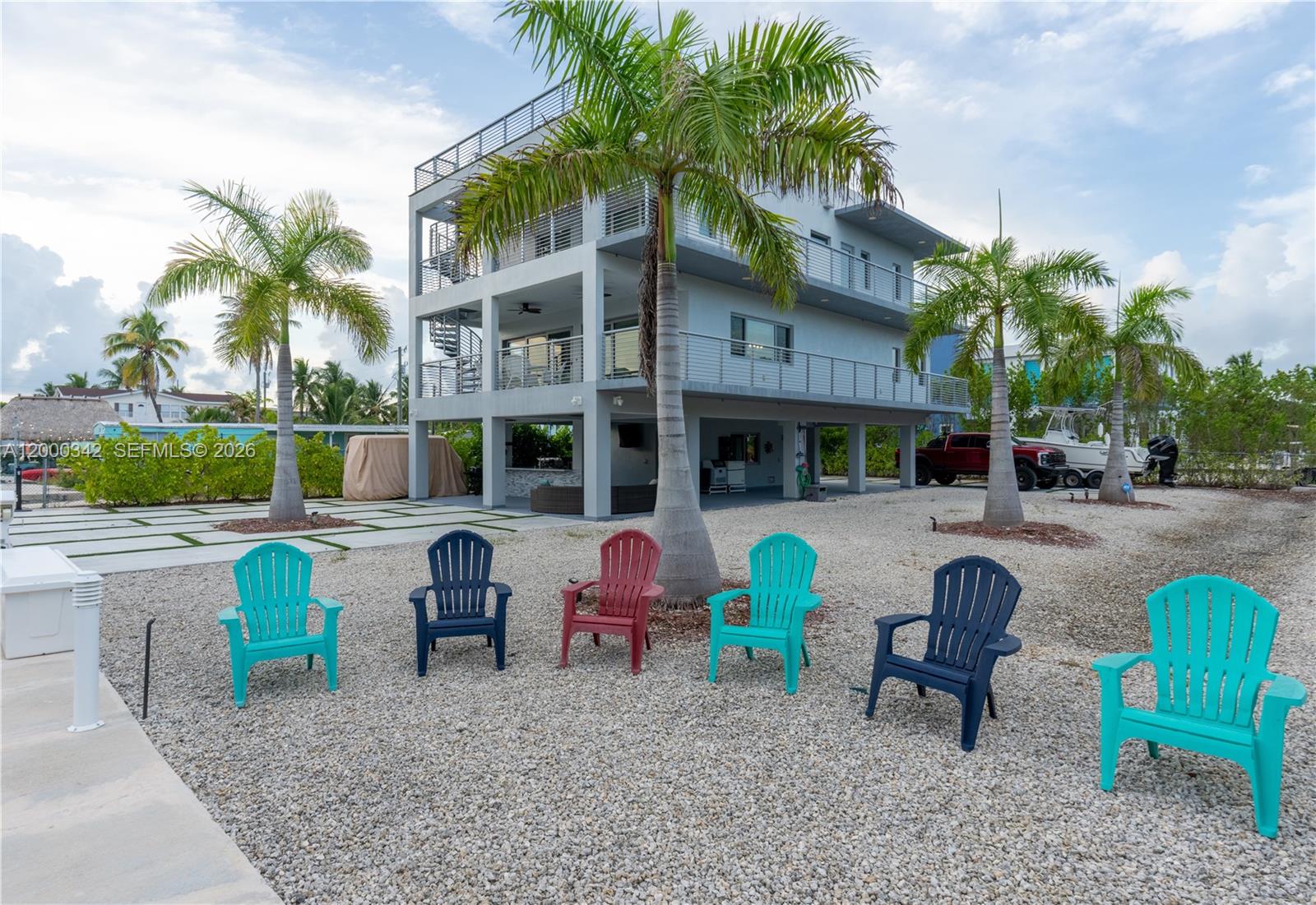 A three-story house stands on stilts above a gravel yard with six colorful Adirondack chairs — 475 Bahia Honda Rd, Key Largo FL 33037, KEY LARGO, FL