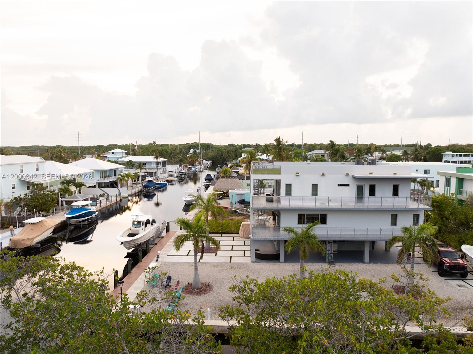 An elevated modern house sits beside a canal filled with boats and palm trees — 475 Bahia Honda Rd, Key Largo FL 33037, KEY LARGO, FL