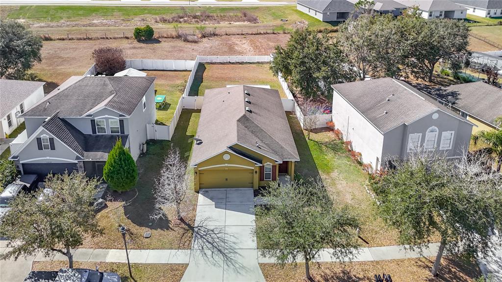 An aerial view shows a yellow single-story house situated between two larger two-story homes — 13221 WATERFORD CASTLE DRIVE, DADE CITY, FL