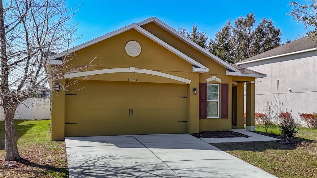 A single-story house with a yellow stucco exterior, a two-car garage, and a front window — 13221 WATERFORD CASTLE DRIVE, DADE CITY, FL