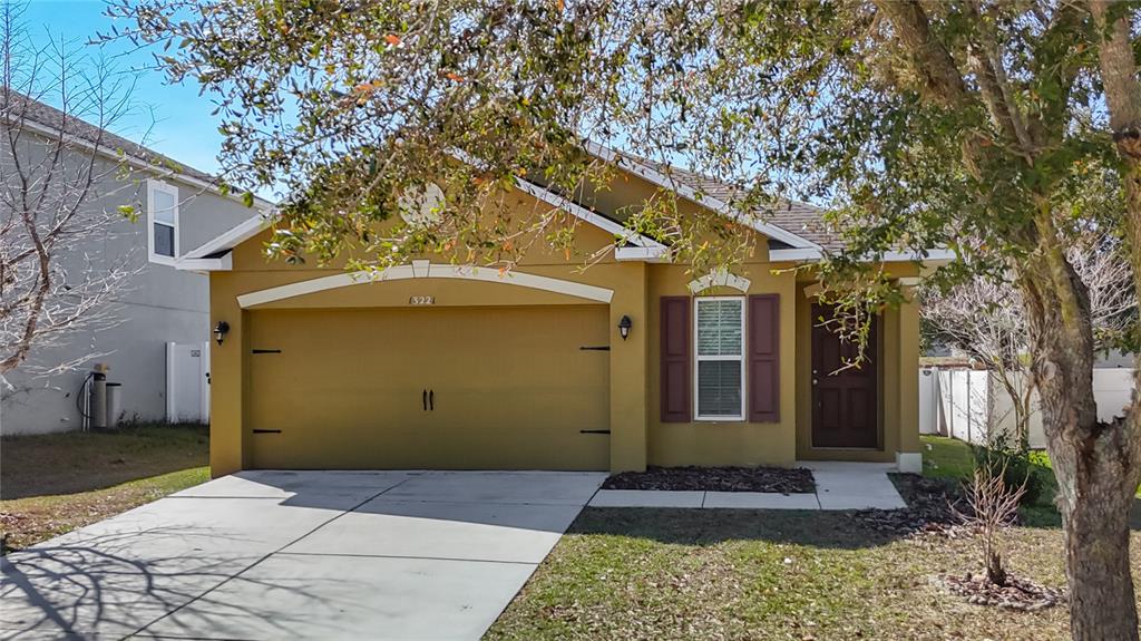 A single-story house with a mustard-colored exterior, a two-car garage, and a brown front door — 13221 WATERFORD CASTLE DRIVE, DADE CITY, FL