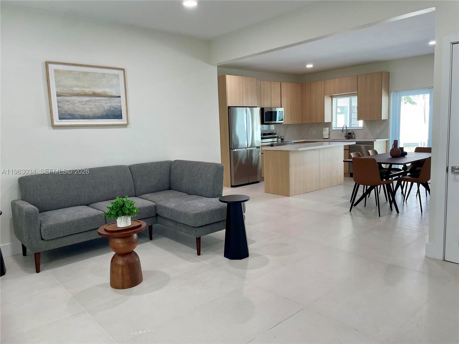 An open-concept living area features a gray sectional sofa, light wood cabinets, and tile flooring — 5352 Orduna Dr # 0, Coral Gables FL 33146, CORAL GABLES, FL