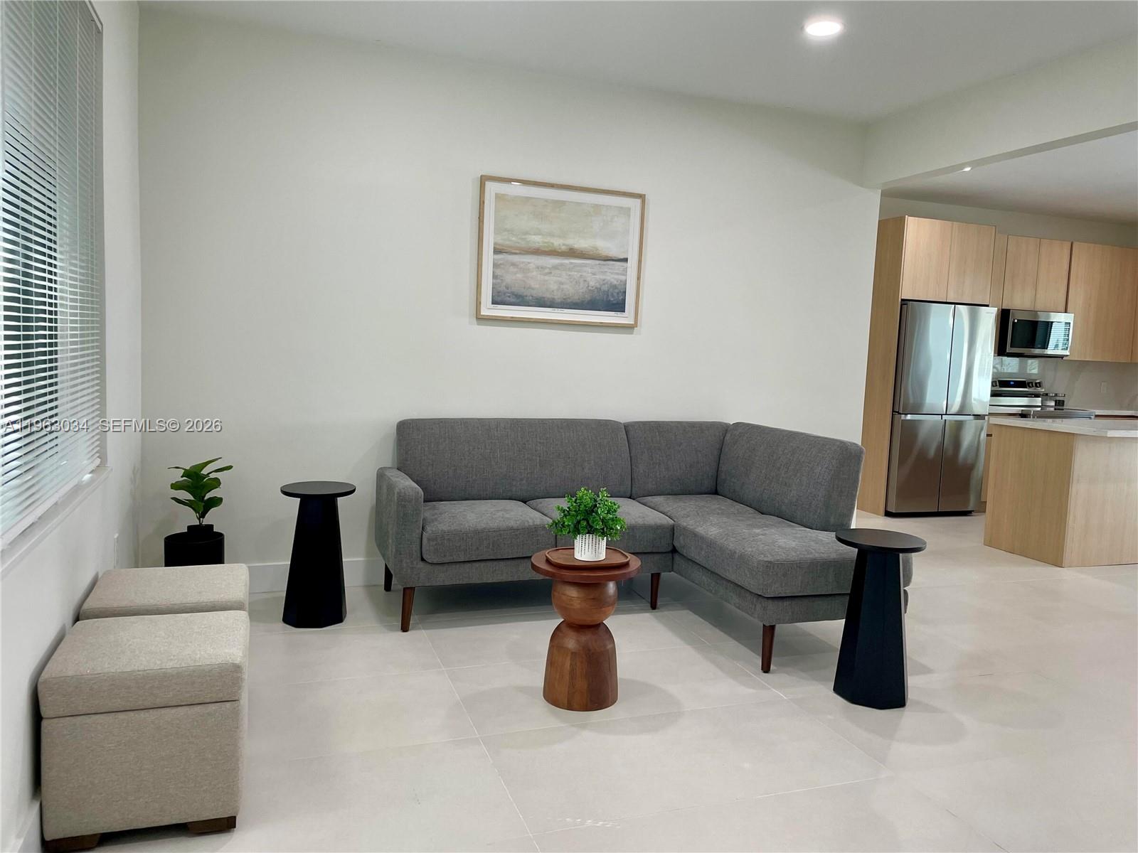 A living room features a gray sectional sofa, a wooden side table, and light tile flooring — 5352 Orduna Dr # 0, Coral Gables FL 33146, CORAL GABLES, FL