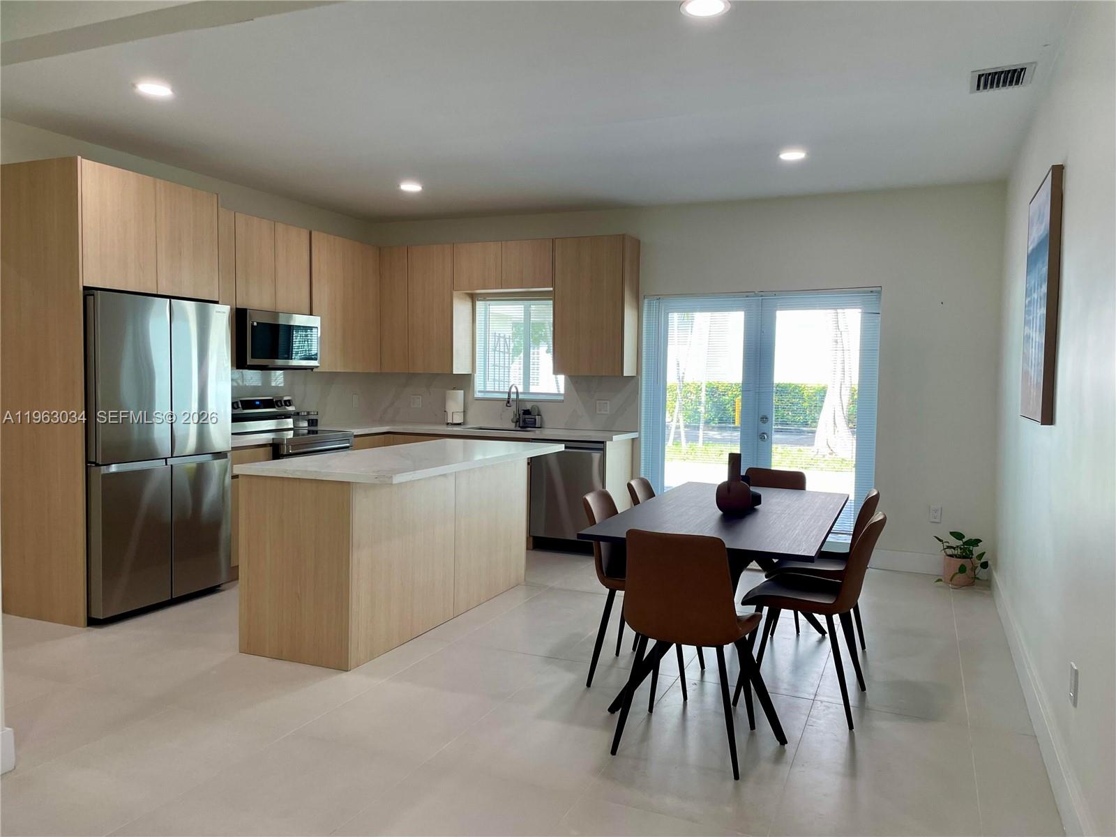 A modern kitchen with light wood cabinets, stainless steel appliances, and an adjacent dining area — 5352 Orduna Dr # 0, Coral Gables FL 33146, CORAL GABLES, FL
