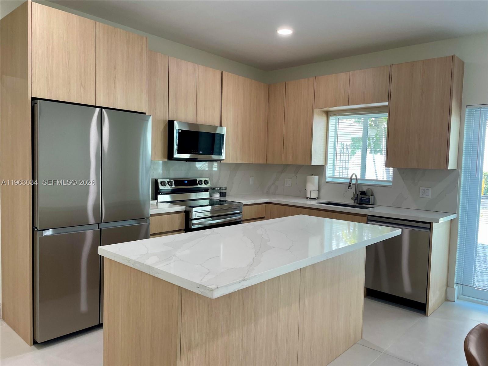 A modern kitchen features light wood cabinets, stainless steel appliances, and a marble-topped island — 5352 Orduna Dr # 0, Coral Gables FL 33146, CORAL GABLES, FL