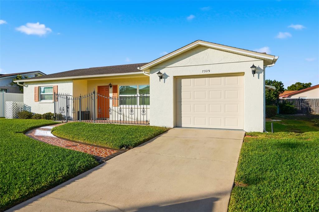 A single-story house with a white stucco exterior, a one-car garage, and a paved walkway — 7329 CAY DRIVE, PORT RICHEY, FL