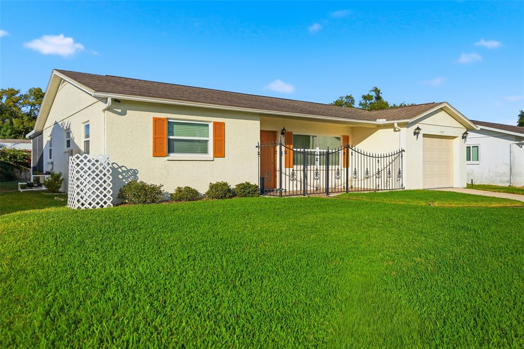 A single-story house with a light-colored exterior, orange shutters, and a front metal fence — 7329 CAY DRIVE, PORT RICHEY, FL
