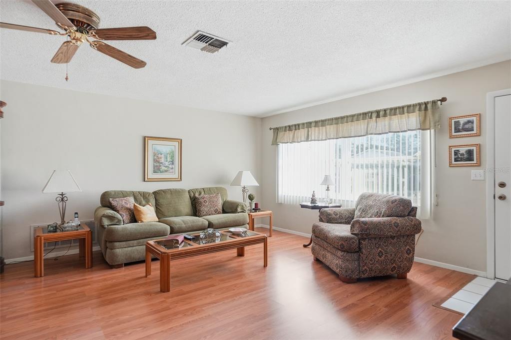 A living room features wood-look flooring, a green sofa, a patterned armchair, and a ceiling fan — 7329 CAY DRIVE, PORT RICHEY, FL